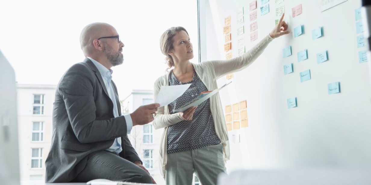 An image of a woman pointing to a sticky note during a business meeting.