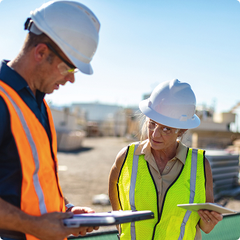 Construction site workers collaborating, safety vests, hard hats, teamwork, outdoor building project, engineering professionals, site management, construction industry, project planning, tablet and clipboard in use.
