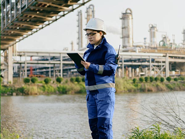 Industrial worker in blue uniform conducting inspection at a manufacturing plant by the river.