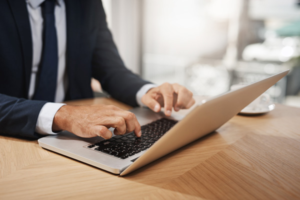 person in a suit typing on a laptop at a wooden table