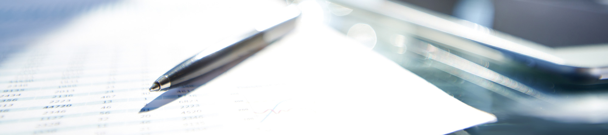 close-up of a pen resting on a sheet of paper with printed data, with a tablet partially visible in the background