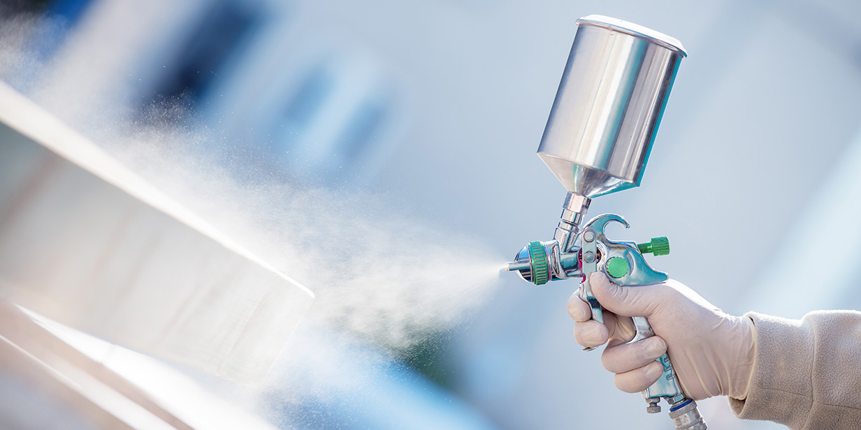 industrial spray finishing process with a worker applying protective coating using a handheld spray gun