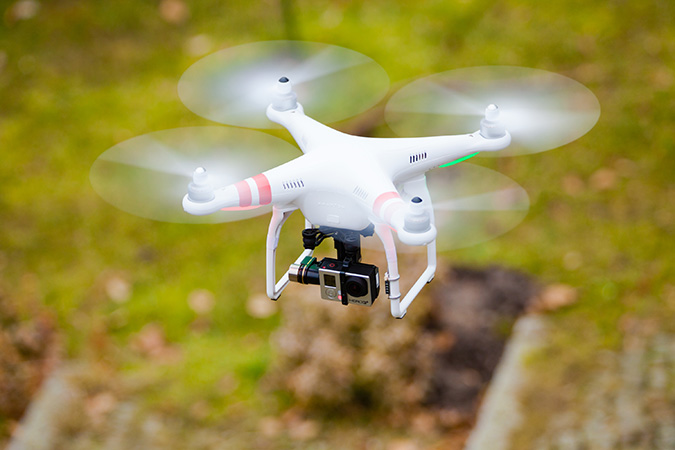 white quadcopter drone with camera flying over grassy terrain