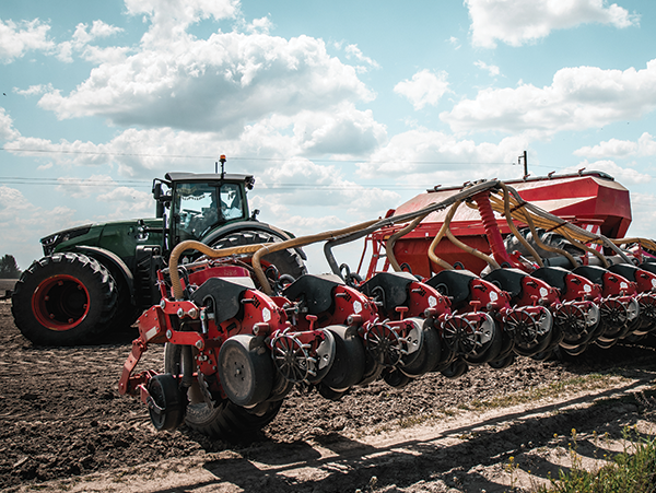 green tractor with red seed planting machine in a field under partly cloudy sky